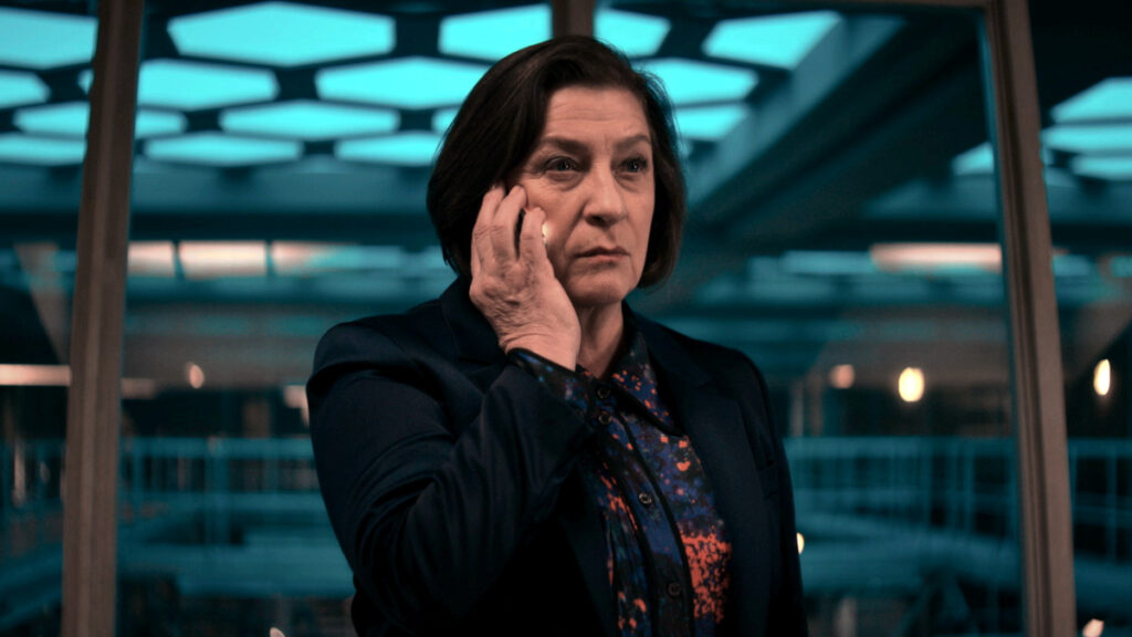 Eine Frau hält ein Handy am Ohr. Sie steht vor einer Glasfront. 