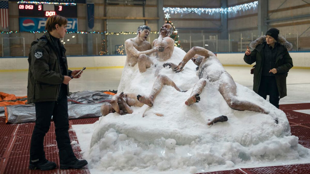 Zwei Polizisten stehen neben einem Schneehaufen aus dem grotesk verrenkt Leichen herausragen.