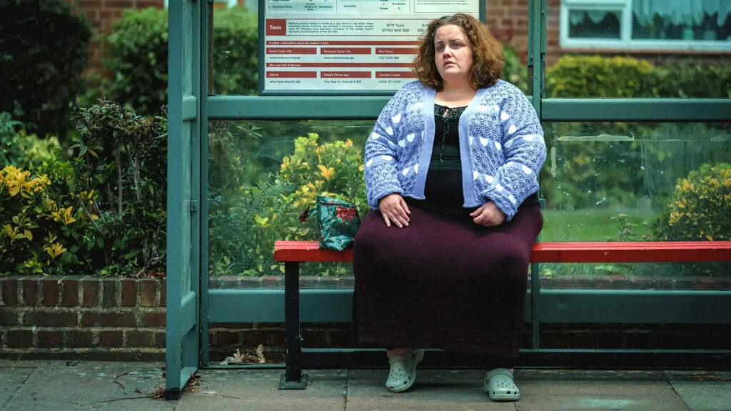 Eine Frau sitzt auf der Wartebank einer Busstation.